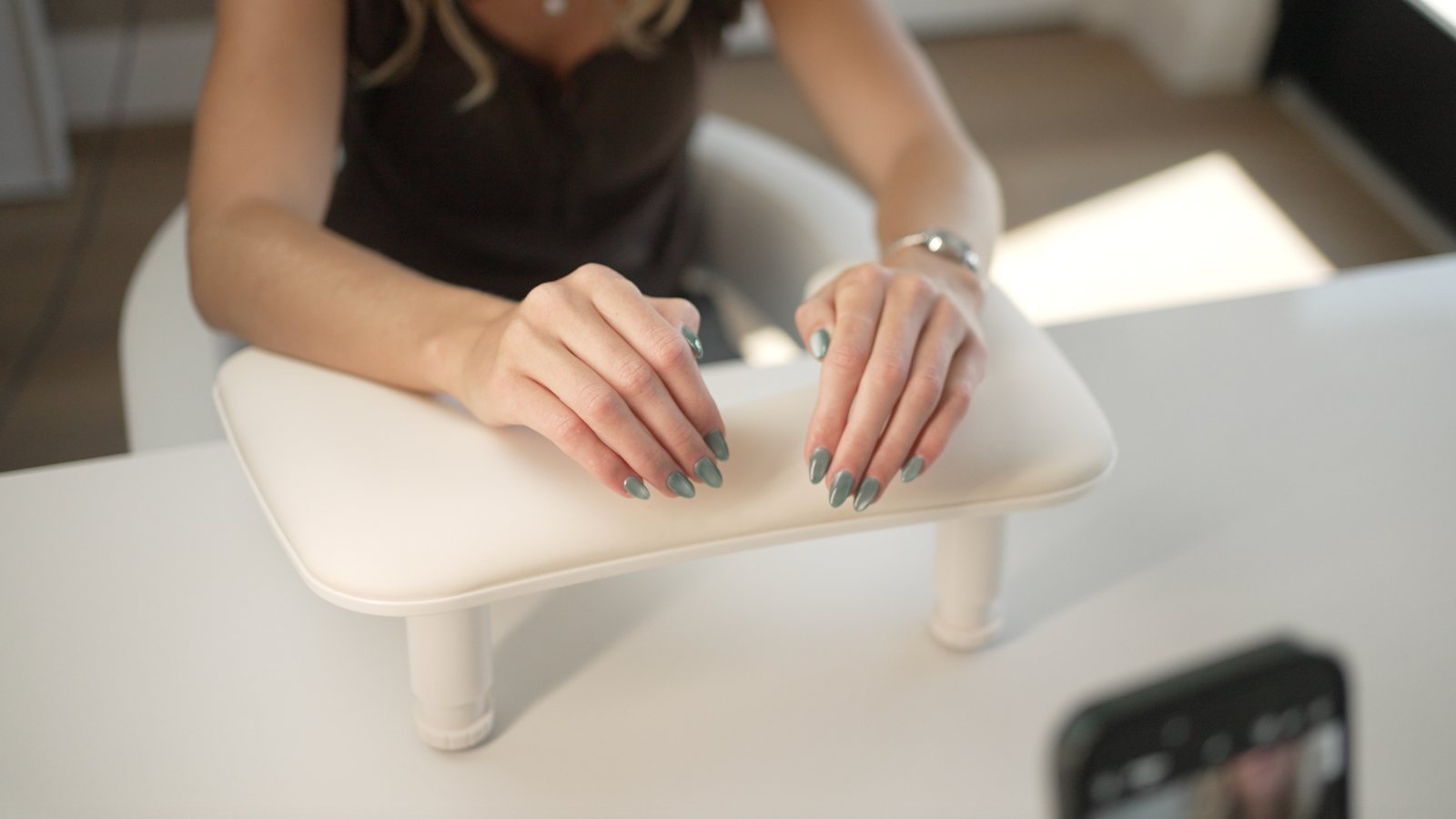 A client's hands resting on a manicure cushion, nails finished in a soft sage green.